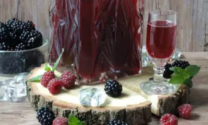 Aromatyczna nalewka ratafia w karafce i kieliszku, otoczona świeżymi malinami, jeżynami i kostkami lodu.