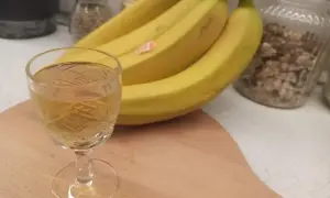Szklaneczka z nalewką z banana obok kiści żółtych bananów.