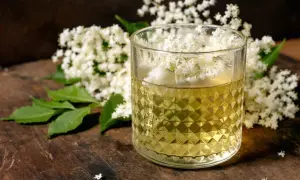 Szklanka z syropem z kwiatów czarnego bzu, obok bukiet kwiatów. Pamiętaj o przeciwwskazaniach do jego spożywania.