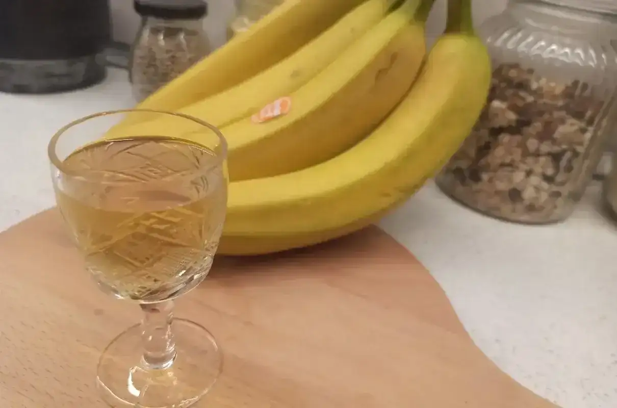 Szklaneczka z nalewką z banana obok kiści żółtych bananów.
