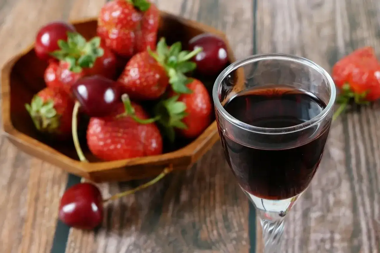 Szklaneczka nalewki ratafia obok miski pełnej truskawek i wiśni.