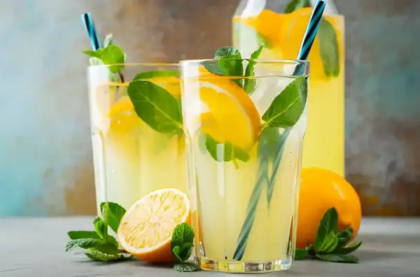 Orzeźwiająca lemoniada z limonki z plasterkami cytryny i listkami mięty w szklankach i dzbanku.