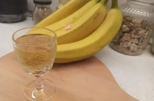 Szklaneczka z nalewką z banana obok kiści żółtych bananów.
