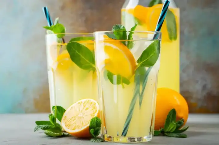Orzeźwiająca lemoniada z limonki z plasterkami cytryny i listkami mięty w szklankach i dzbanku.